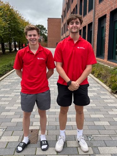 Two Sixth Form boys standing proudly side by side wearing matching red polo shirts 